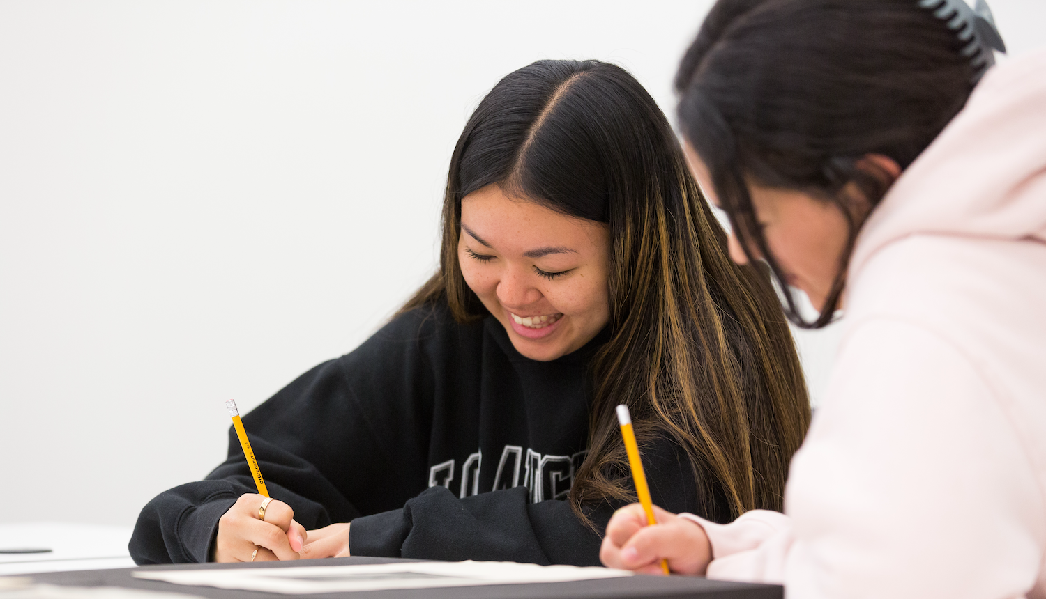 Two students writing and smiling in class